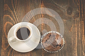 Cup of black coffee and a chocolate muffin/cup of black coffee and a chocolate muffin on a dark wooden table. Top view and