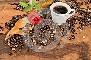 A cup of black coffee with coffee beans and red rose