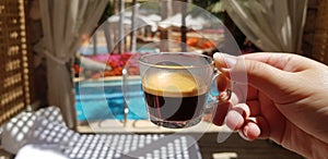 Cup with black coffee in female hand against a view from luxury hotel room