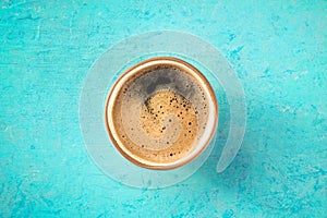 A cup of black coffee with froth, overhead flat lay shot on blue