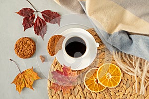 Cup of black coffee on a gray background with autumn leaves, a warm cape, a wicker napkin, oatmeal cookies and slices of dried