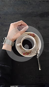 A cup of black coffee, a hand side by side with a cup of coffee on a black table,bitter coffee