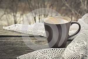 Cup of black coffee with milk in front of the window and a lace on the wooden background.