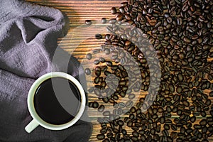 Cup of black coffee  and napkin with beans on old kitchen wooden table.