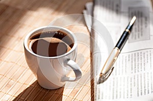 Cup of black coffee, newspaper and a pen