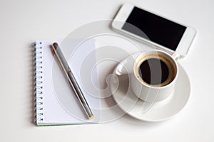 cup of black coffee, note book, silver pen and white smartphone on white background