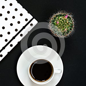 Cup of black coffee, notebook and blooming cactus on black background, Top view, copy space