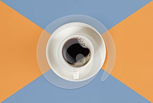 A cup of black coffee on orange and blue background. View from above.