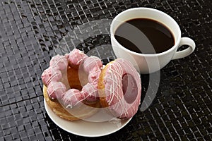 Cup of black coffee with pink donuts