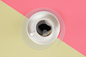 A cup of black coffee on pink and yellow background. View from above.