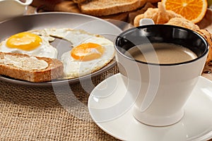 Cup of black coffee, plate with fried eggs and toast with butter