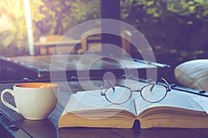 A cup of black coffee with reading glasses on table and open boo