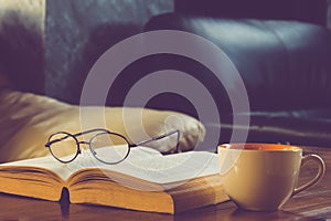 A cup of black coffee with reading glasses on table and open boo