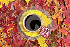 Cup with black coffee, red, yellow lollipops on wooden table with autumn fallen yellow, orange and red leaves