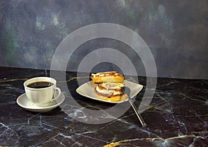 A cup of black coffee on a saucer and bwe cinnamon rolls on a plate, next to a fork