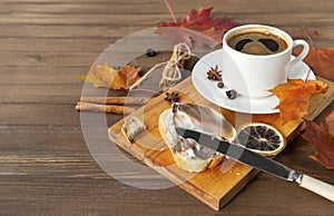 Cup of black coffee with a saucer, orange autumn maple leaves, cinnamon sticks, anise stars ,a piece of bread with creamy