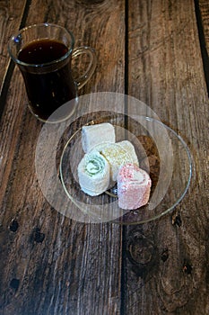 A cup of black coffee with a spoon on a wooden table and oriental sweets on a saucer. Close-up