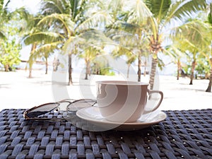 A cup of black coffee and sun glasses with coconut tree plan on white sand beach sea view background, Travel plans after