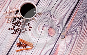 A cup of black coffee, wafer rolls, cinnamon sticks, anise and roasted coffee beans lie on a wooden table