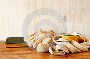 Cup of black coffee with a warm scarf and old book on wooden background. filreted image