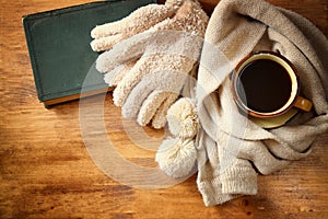 Cup of black coffee with a warm scarf and old book on wooden background. filreted image.
