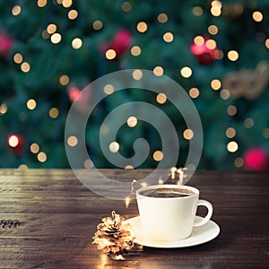 Cup of black coffee on wooden table in cafe. Christmas lights and gold garland on background.