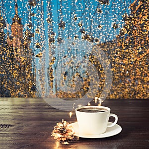 Cup of black coffee on wooden table in cafe. Christmas lights and gold garland on background