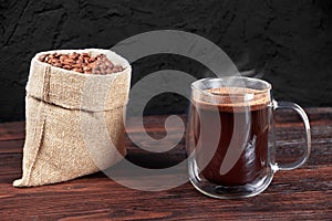 A cup of black coffee on wooden table. A glass mug of coffee. Coffee beans in bag on wooden background. Morning coffee