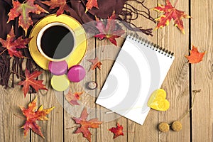 Cup with black coffee, yellow lollipops, macaroons, textile scarf, notepad, wooden table with autumn fallen orange leaves