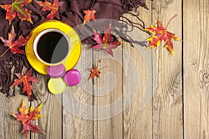 Cup with black coffee, yellow lollipops, macaroons, textile scarf, notepad, wooden table with autumn fallen orange leaves