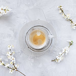 Cup of black espresso coffee and white spring cherry blossom flowers on gray background, copy space