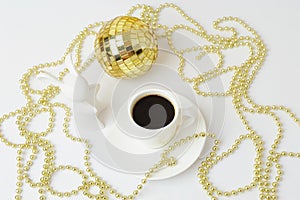 Cup of black espresso and white ceramic rabbit. Symbol of the year. Gold Christmas beads and disco ball