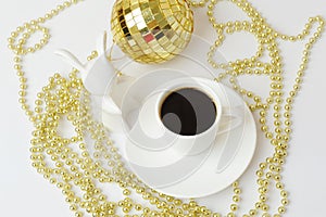 Cup of black espresso and white ceramic rabbit. Symbol of the year. Gold Christmas beads and disco ball