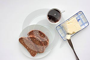 Cup of black herbal tea, slices of dark rye and whole wheat bread with sesame seeds and butter on a plate on white table