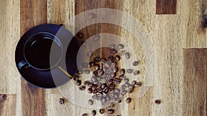 Cup of black morning coffee and cofee beans scattered on brown wooden table