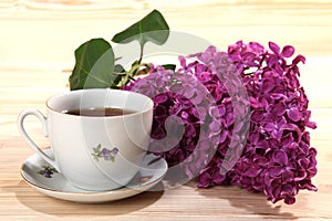 Cup of black tea and branch of lilacs on wooden background