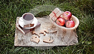 A cup of black tea, ginger cookie and a basket with red apples. Autumn harvest.