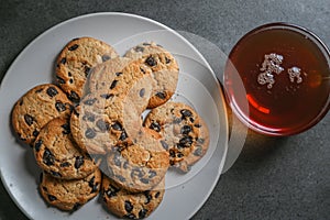 A cup of black tea in a glass cup and a gray ceramic plate with cookies with chocolate chips on a gray ceramic tabletop