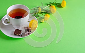 A Cup of black tea, pieces of chocolate and yellow flowers of Trollius europaeus on a green background. Chocolate day