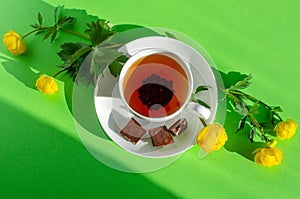 A Cup of black tea, pieces of chocolate and yellow flowers of Trollius europaeus on a green background. Chocolate day