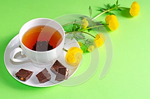 A Cup of black tea, pieces of chocolate and yellow flowers of Trollius europaeus on a green background. Chocolate day