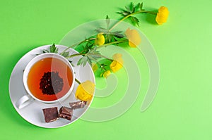A Cup of black tea, pieces of chocolate and yellow flowers of Trollius europaeus on a green background. Chocolate day