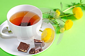 A Cup of black tea, pieces of chocolate and yellow flowers of Trollius europaeus on a green background. Chocolate day