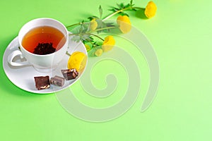 A Cup of black tea, pieces of chocolate and yellow flowers of Trollius europaeus on a green background. Chocolate day