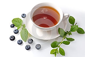 A Cup of black tea on a saucer with mint leaves and blueberries on a white background