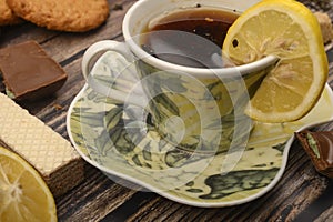 A Cup of black tea, sliced lemon, brown sugar slices, oatmeal cookies, waffles on a wooden background. Close up