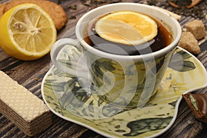 A Cup of black tea, sliced lemon, brown sugar slices, oatmeal cookies, waffles on a wooden background. Close up