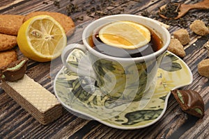 A Cup of black tea, sliced lemon, brown sugar slices, oatmeal cookies, waffles on a wooden background. Close up