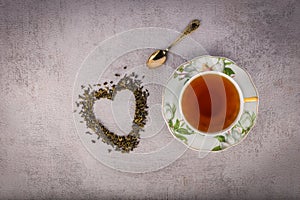 Cup of black tea, small antique spoon and heart-shaped scattered tealeaves