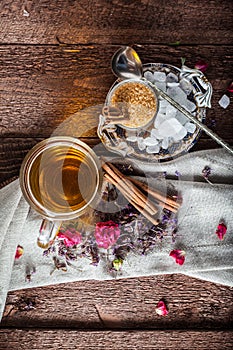 Cup of black tea with sugar cane, roses, tea leaves on a brown wooden background